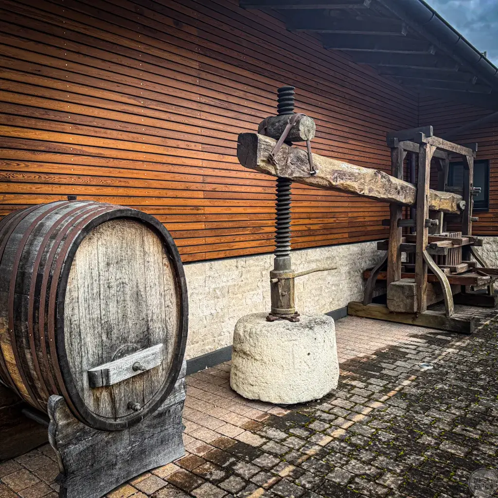 A historic wine press and old barrel outside the wooden distillery building